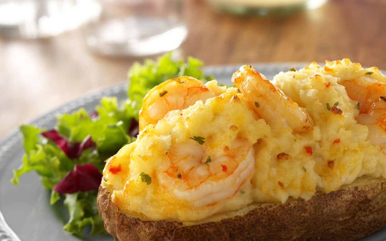 A Loaded Taters baked potato topped with shrimp, creamy sauce and melted cheese